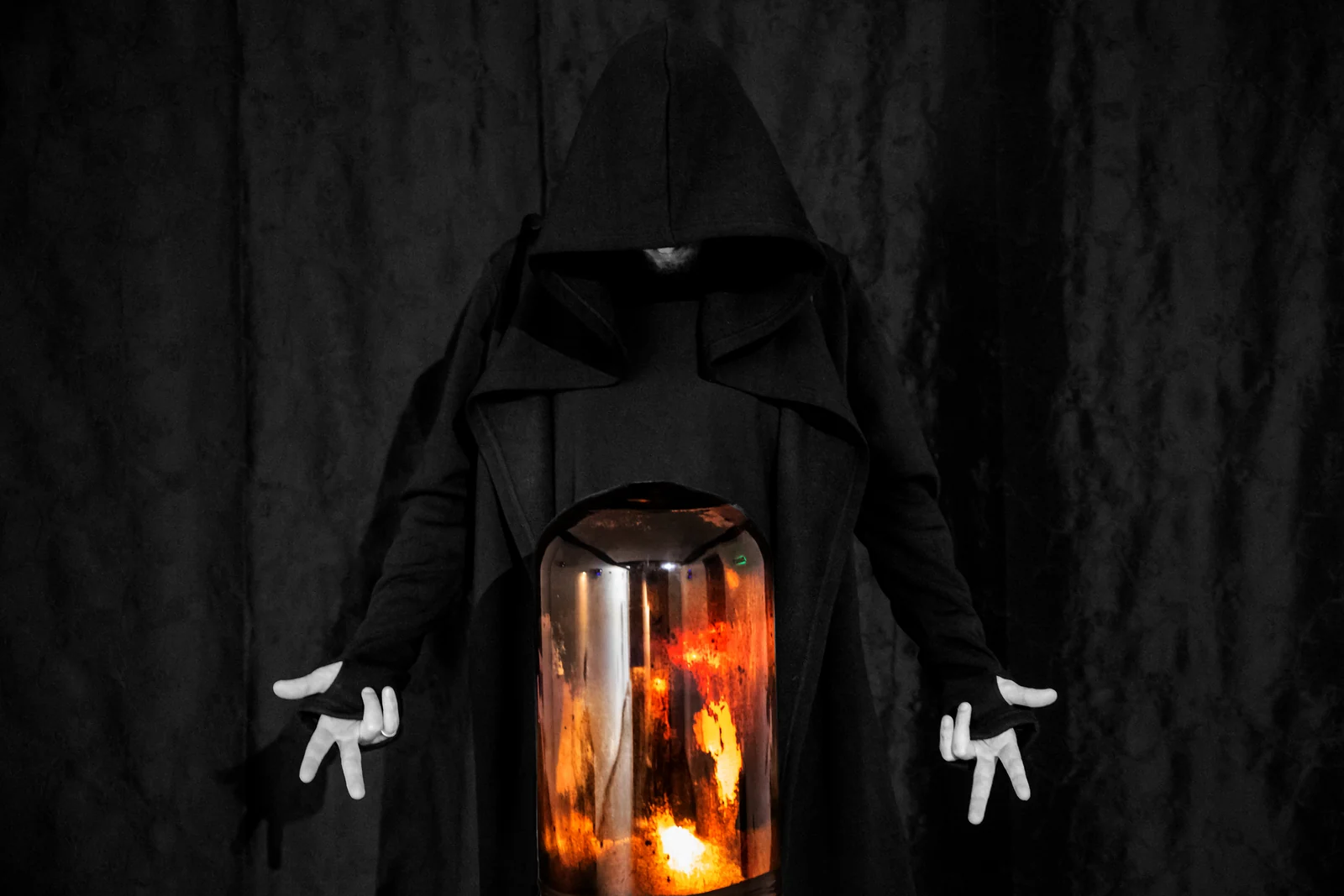 Deus Ex Machina — a hooded figure holding a glowing vessel of fire, the central image of the series